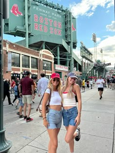 two women standing next to each other in front of a baseball stadium with boston red sox sign