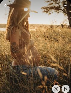 a woman sitting in the grass wearing a cowboy hat