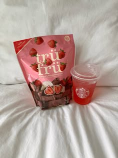 a bag of strawberries next to a cup of coffee on a white bed sheet