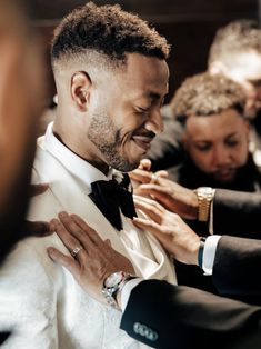 a man in a tuxedo smiles as he puts his hands together