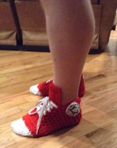 a person wearing red and white crocheted shoes on top of a hard wood floor