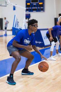 a young man holding a basketball on top of a hard wood floor in a gym