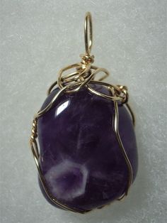 Amethyst Pendant Wire Wrapped in 14/20 Gold Filled Round Wire This ennobling stone provides subtle shades of light to dark translucent purple with some white coloration. It especially compliments pink, lavender, yellow, red, burgundy, and blue colors of clothing, though probably best worn with light or dark color contrast combinations. Although the rather consistent color might appeal to a purist view; the imperfect shape, angular crystal plane pattern, and natural slightly pitted surface along Purple Oval Spiritual Jewelry, Gold Amethyst Gemstones For Healing, Spiritual Purple Oval Jewelry, Spiritual Oval Purple Jewelry, Purple Jewelry With Large Stone For Healing, Oval Purple Gemstones For Gifts, Deep Purple Color, Shades Of Light, Stone Wrapping