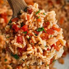 a wooden spoon filled with rice and tomatoes