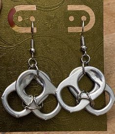 a pair of silver metal earrings sitting on top of a wooden table next to a book