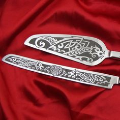 two silver serving utensils with intricate designs on red satin background, closeup