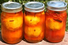 three jars filled with pickles sitting on top of a wooden table