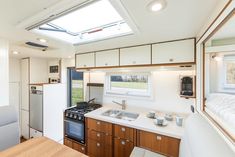 a kitchen and living area in a tiny home with skylights above the sink, stove top oven and refrigerator