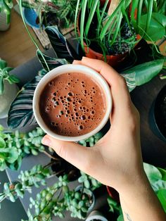 a person holding a coffee cup in front of some plants