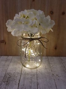 a mason jar filled with white flowers on top of a wooden table