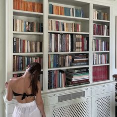 a woman standing in front of a book shelf filled with books