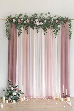 a pink and white wedding backdrop with flowers, candles and greenery on the floor