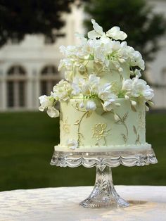 a three tiered cake with white flowers on the top is sitting on a table