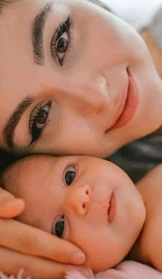 a woman holding a baby in her arms while laying on top of a bed next to it