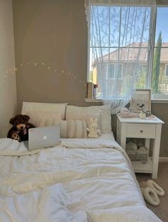 a laptop computer sitting on top of a white bed in a bedroom next to a window