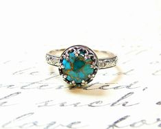 "Beautiful handmade ring. Constructed completely in sterling silver. The gemstone is actually a 8 mm round blue copper turquoise stone. The band of the ring has a lovely repeating floral pattern on it. The bezel is made to look like upside down hearts holding a unique stone. All these details put together give it a look of \"Gothic Renaissance\". This ring is so lovely. Rings are \"made to order\". Generally it will take 2-3 days to complete unless there is a \"special request\" involved. Buyers Handmade Turquoise Wedding Ring, Turquoise Round Jewelry With Stone Setting, Turquoise Sterling Silver Ring With Bezel Setting, Turquoise Round Stone Setting Jewelry, Round Turquoise Jewelry With Stone Setting, Heirloom Style Turquoise Cabochon Ring, Heirloom Turquoise Cabochon Ring, Bohemian Jewelry With Bezel Setting In Round Shape, Bohemian Round Jewelry With Bezel Setting