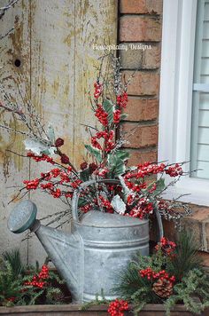 a metal watering can with red berries and greenery in front of a brick building