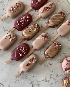 chocolate covered desserts on sticks with sprinkles and toppings are arranged on a marble surface