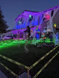 halloween decorations on display in front of a large house at night with neon tape around the yard