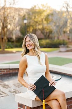 a woman is sitting on a brick wall with her graduation cap and gown in hand