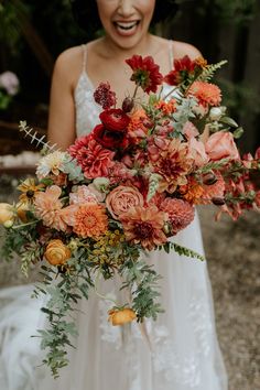 a bride holding a bouquet of flowers in her hands and laughing at the camera man