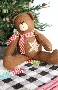 a brown teddy bear sitting on top of a quilt