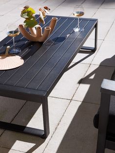 a table that has some wine glasses and a vase with flowers on it sitting outside