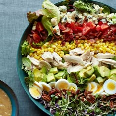 a salad with hard boiled eggs, tomatoes, avocado, corn and dressing