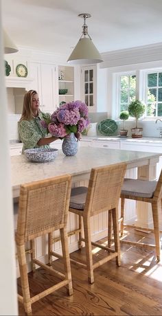 a woman sitting at a kitchen island with flowers in a bowl on the counter top