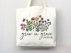 a white tote bag with flowers and the words grow in grace written on it