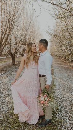 a man and woman standing next to each other in front of some trees with flowers