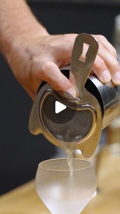 a person pours liquid into a glass with a strainer in their left hand