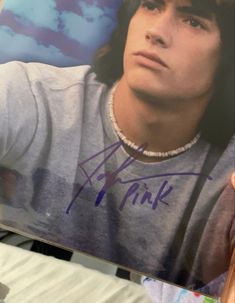 a young man holding up a signed photo in front of the camera with his name on it