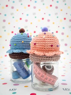 two crocheted hats are sitting in small jars with tape and scissors on them