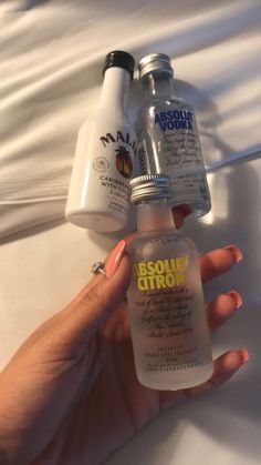 a hand holding two bottles of liquid next to each other on top of a bed