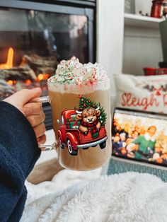 a person holding up a drink in front of a fire place with christmas decorations on it