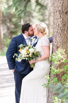 a bride and groom kissing by a tree in the woods on their wedding day photo