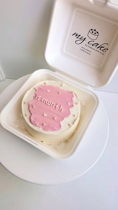 a pink frosted cake sitting on top of a white plate next to a plastic container