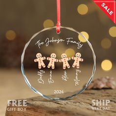 a glass ornament with three ginger family members on it, hanging from a red ribbon