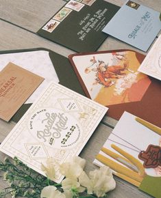 several different types of wedding cards and envelopes on a table with flowers in the foreground