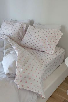 a bed with white sheets and pink hearts on it's pillow cases, along with two night stands