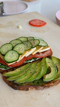 a sandwich with cucumber and tomato slices on it sitting on a cutting board