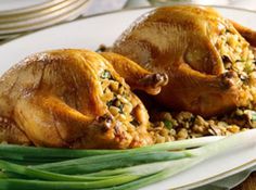 two whole chickens on a white plate with green beans and rice as garnish