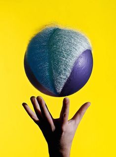 a person's hand reaching up to catch a blue and green ball on a yellow background