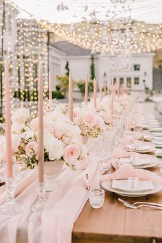 the table is set with pink and white flowers in vases, candles, and place settings