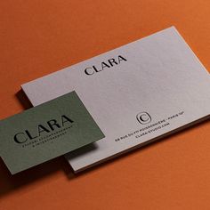 two business cards sitting on top of an orange surface with the word clara printed on them