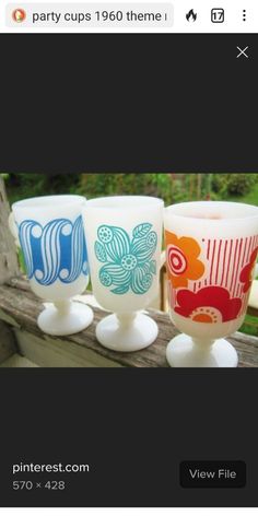 three cups sitting on top of a wooden table next to each other and one cup is painted with different colors