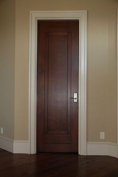 an empty room with a wooden door and hard wood flooring