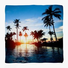 the sun is setting behind some palm trees near a swimming pool with lounge chairs and umbrellas