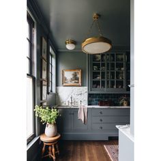 a kitchen with gray cabinets and white counter tops, wooden flooring and a hanging light over the sink